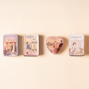 Four illustrated Angelina confectionery tins arranged in a row on a soft beige background.