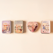 Four illustrated Angelina confectionery tins arranged in a row on a soft beige background.