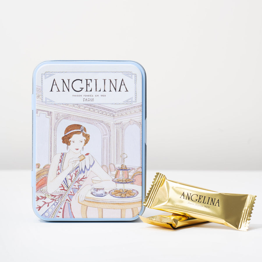 A light blue collectible Art Deco tin from Angelina Paris featuring an elegant illustrated woman in a Parisian tearoom, shown alongside individually wrapped dark chocolate crispy crêpes in gold foil packaging.