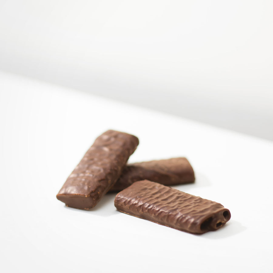 Close-up of three dark chocolate-covered crispy crepe bites with a delicate flaky inside, displayed on a white background.