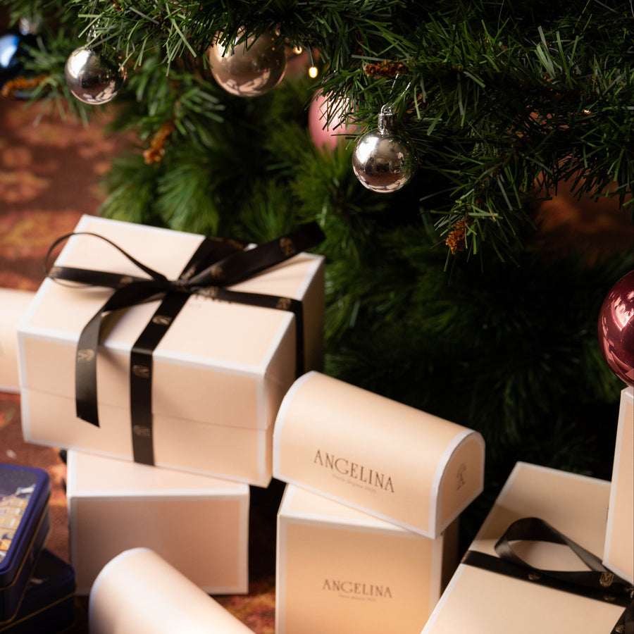 Angelina Paris gift boxes wrapped with black ribbon placed under a decorated Christmas tree.