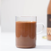 A clear glass mug filled with rich, creamy Angelina Paris signature hot chocolate on a light background.