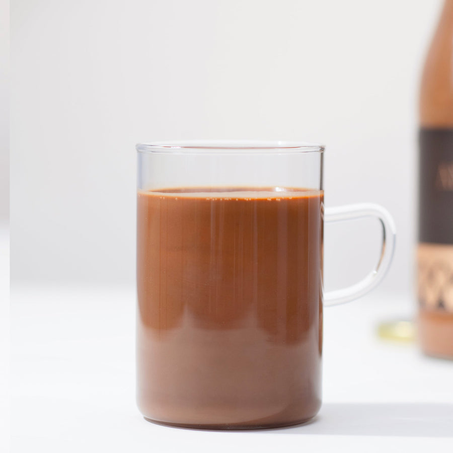 A clear glass mug filled with rich, creamy Angelina Paris signature hot chocolate on a light background.