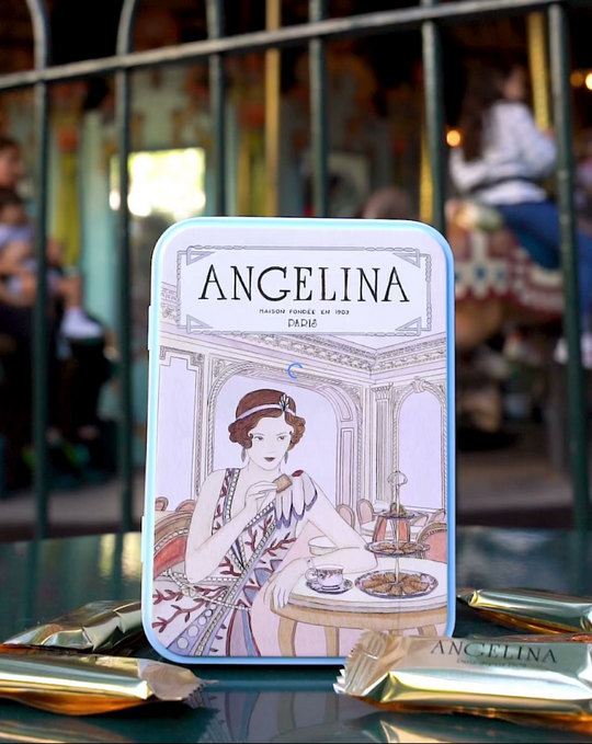 Elegant Angelina Paris collectible tin displayed outdoors, featuring vintage artwork of a woman enjoying pastries, surrounded by individually wrapped dark chocolate crispy crepes.