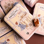 Stacked Angelina tins with a vintage candy shop illustration, with a wrapped caramel placed on top.