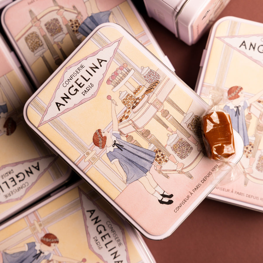 Stacked Angelina tins with a vintage candy shop illustration, with a wrapped caramel placed on top.