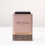 A pale pink metal tea tin from Angelina Paris is displayed on a white surface. The tin features a minimalist Art Deco design with gold and black leaf motifs at the bottom and the text “Mont Blanc Flavoured Black Tea” printed in English and French. It conveys a refined and elegant Parisian aesthetic.